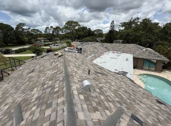 Shingle roof under repair with workers on a residential home near a backyard pool